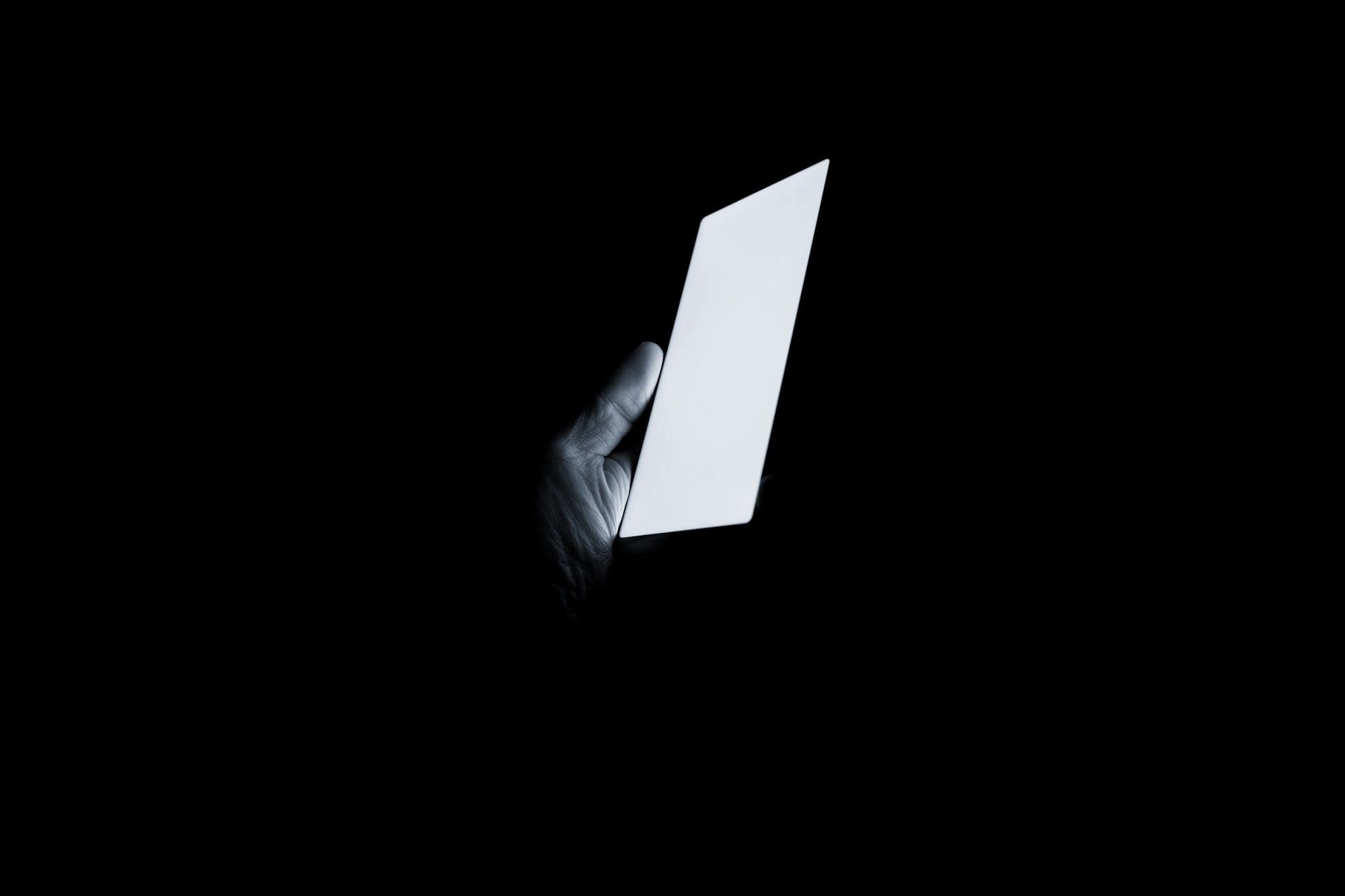A hand holding a glowing smartphone in the dark